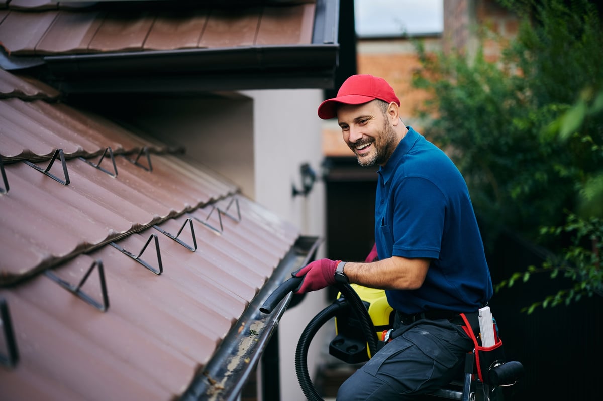 Professional gutter cleaning a house roof with leaf blower